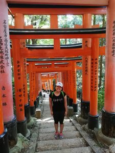 Helen walking along a path through a series of large red wooden gates with Japanese script on them.