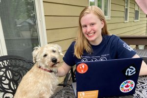 Lauren Streitmatter sitting at a laptop on the patio of a house with while petting a dog.