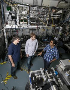 Mohit and two men seen from above in a multi-story lab space with large electronic equipment in the background.