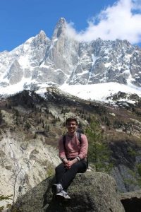 Taylor sitting on a boulder with snow-capped mountains and forest behind him.