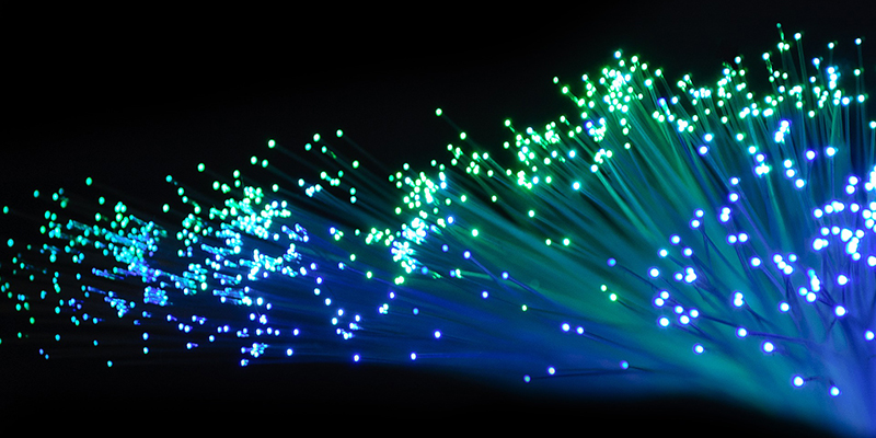 photo of the ends of a bundle of optical fibres glowing with green and blue light against a black background