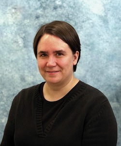 Professor Kaley Walker wearing a black shirt and smiling in front of a light blue background