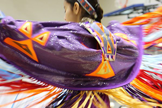 web-UofT16377_shawl-purple-yellow_credit-Hannah-James-600x400 an Indigenous dancer performing with outstretched arms in purple, beaded regalia