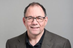 Professor Jonathan Rose wearing a dark grey jacket over a black shirt and dark-rimmed glasses
