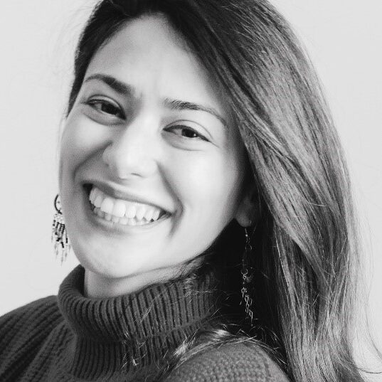 black and white photo of Mandana Esmaeili wearing a turtleneck sweater and smiling to camera